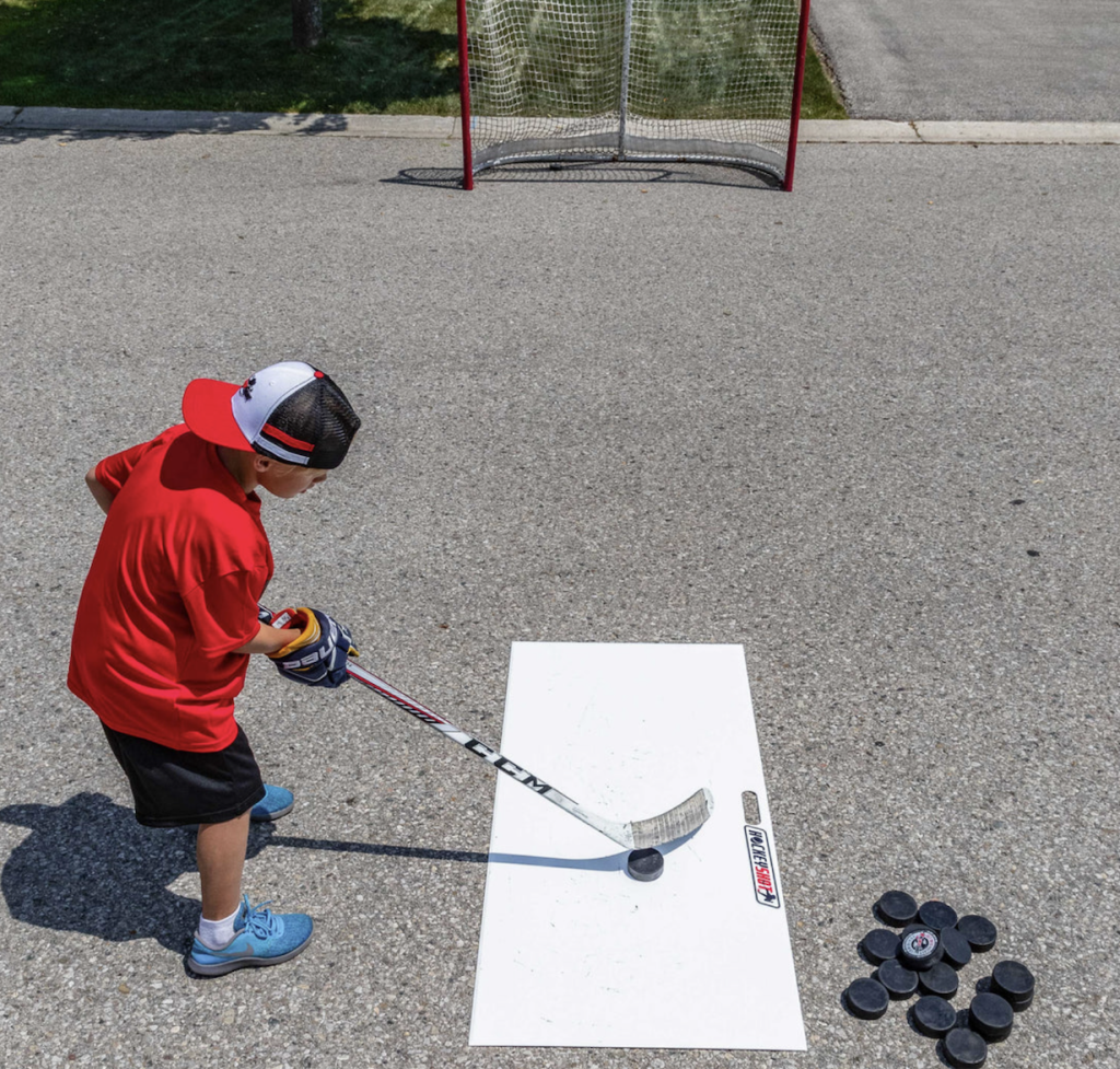 A young hockey player using a slide board to take shots outside.